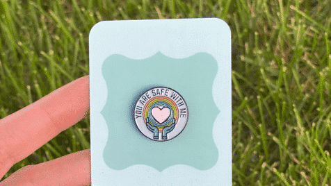 vinyl pin with rainbow and two hands holding a heart and the text you are safe with me, LGBTQ+ pride